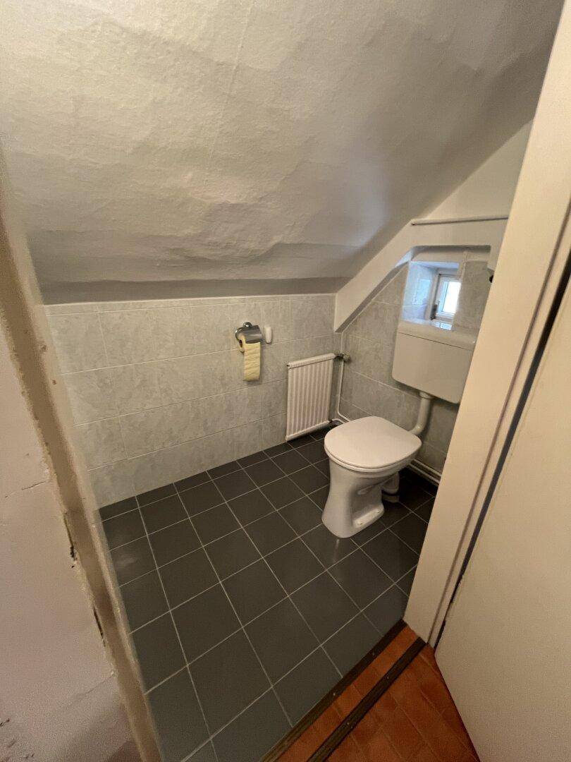 Kleines Gäste-WC im Dachgeschoss mit grauen Fliesen und Fenster.