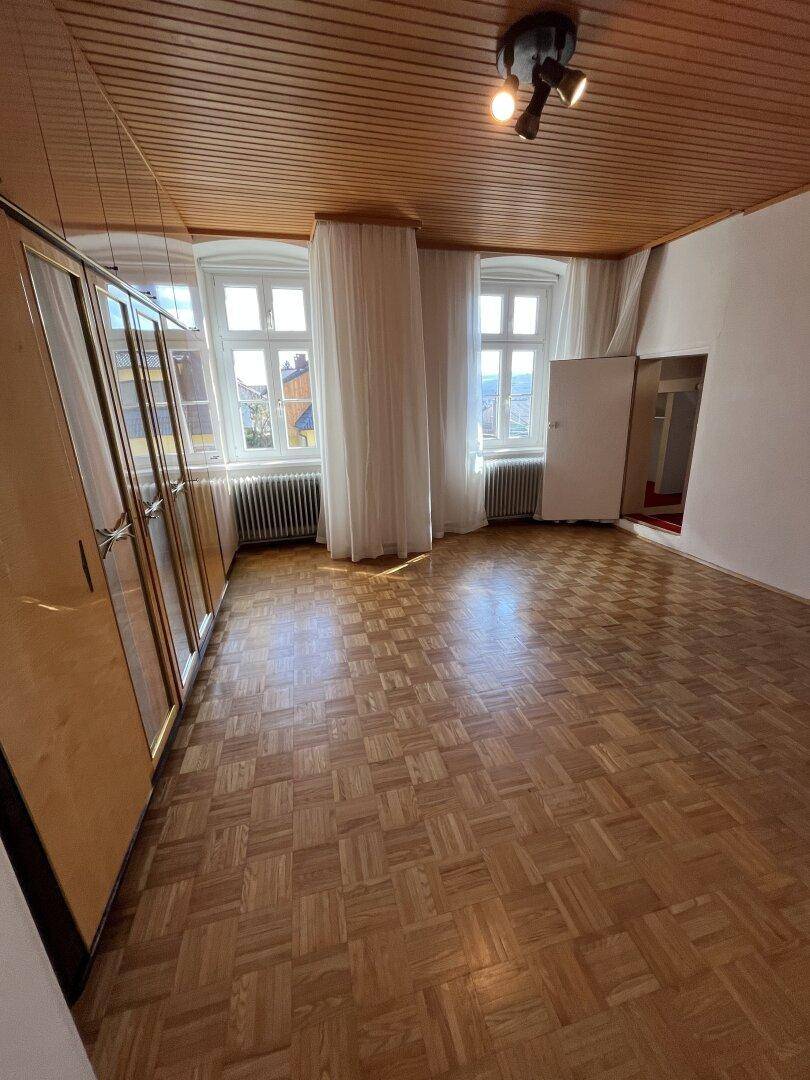 Helles Schlafzimmer mit Parkettboden, Holzdecke und großen Fenstern.