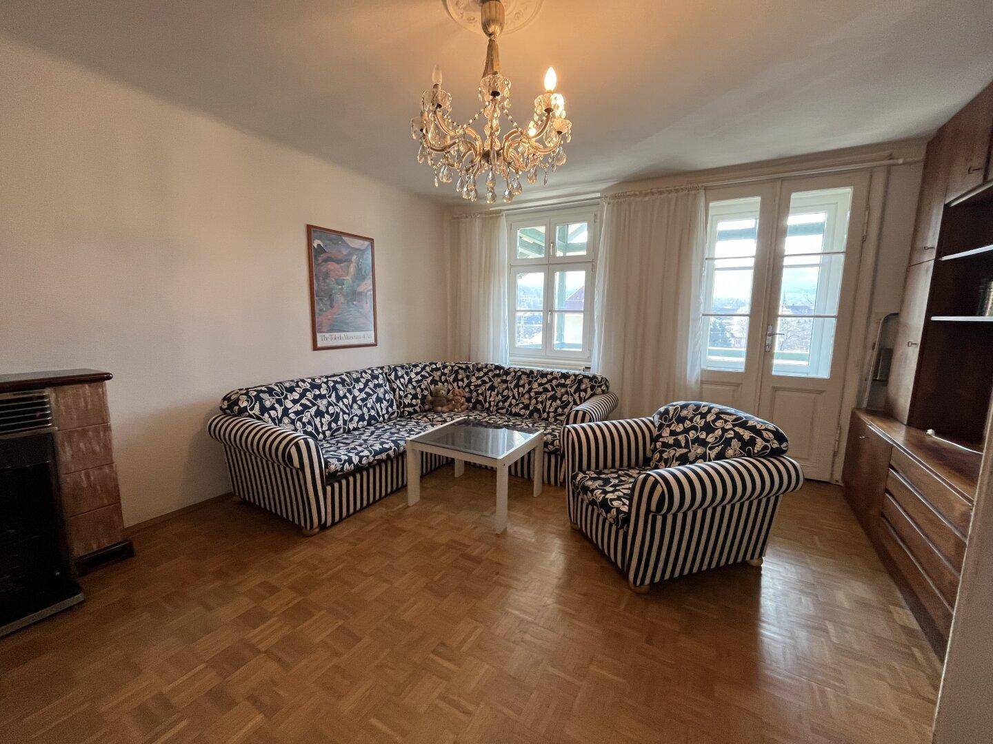 Geräumiges Wohnzimmer mit Parkettboden, gestreiftem Sofa und Kaminofen.