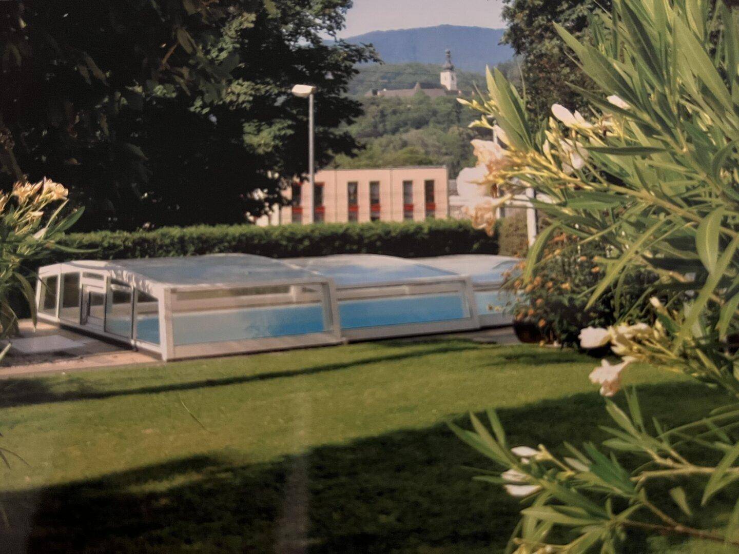 Grüner Gartenbereich mit überdachtem Pool und Blick auf die Umgebung.