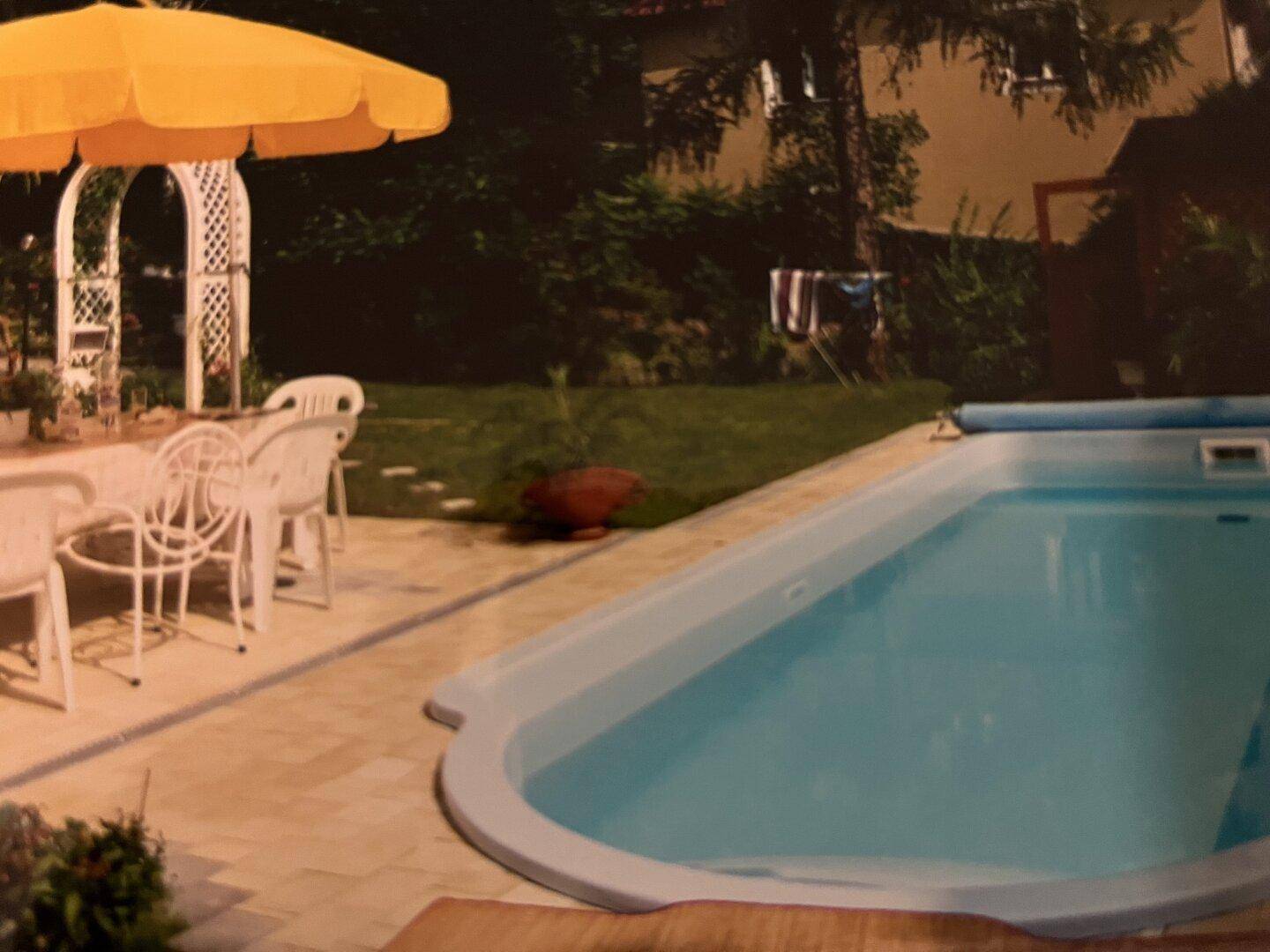 Garten mit Pool, gepflasterter Terrasse und Essbereich im Freien.