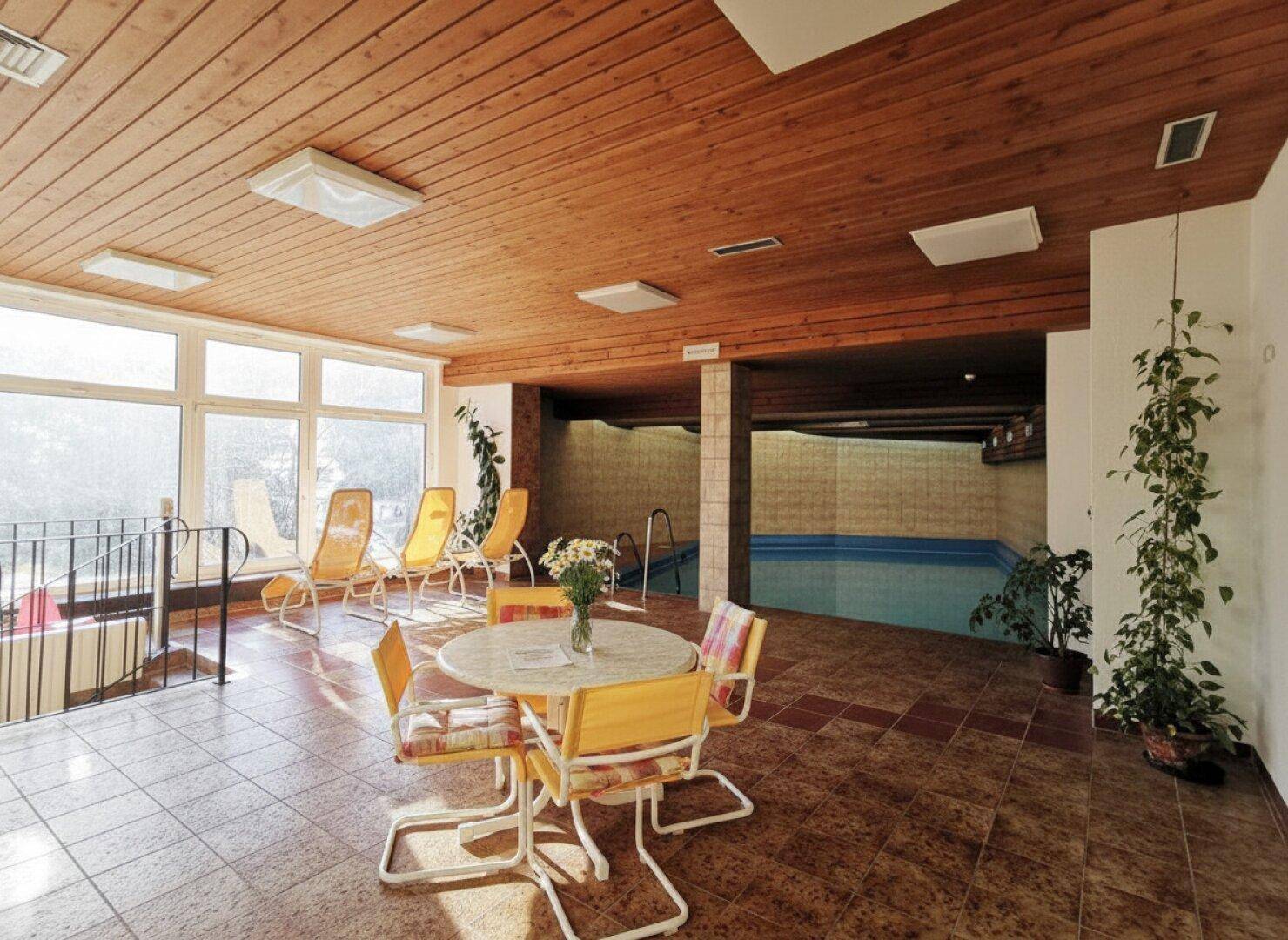 Heller Wellnessbereich mit Innenpool, Liegestühlen und Sitzgelegenheiten unter Holzdecke.