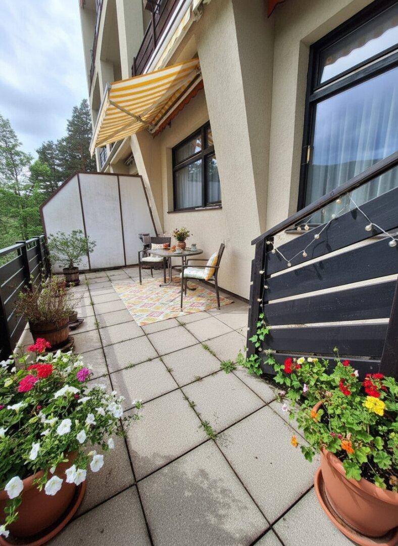 Sonniger Terrassenbereich mit Markise, Gartenmöbeln und Blumen in Töpfen.