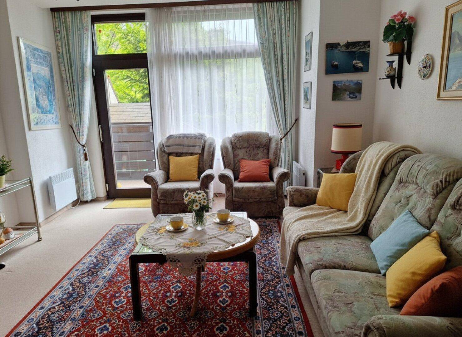Gemütliches Wohnzimmer mit Teppichboden, bequemen Sesseln und Zugang zu einem Balkon.
