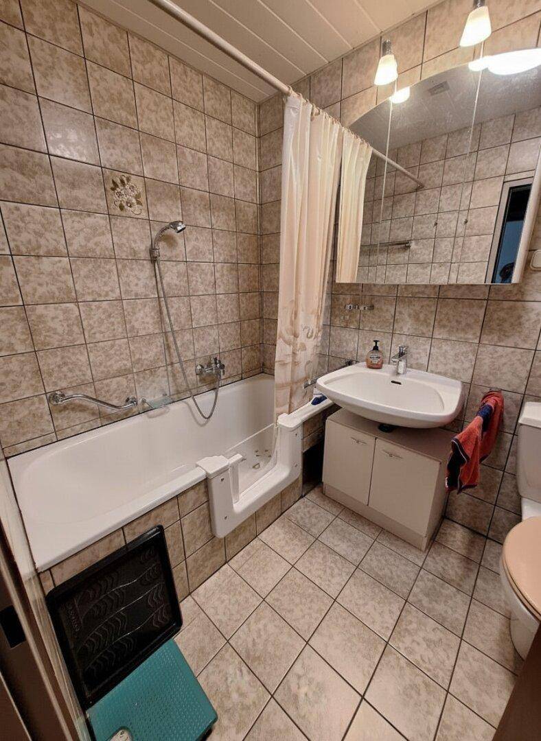 Gefliestes Badezimmer mit Badewanne, integriertem Einstieg und Einzelwaschbecken.