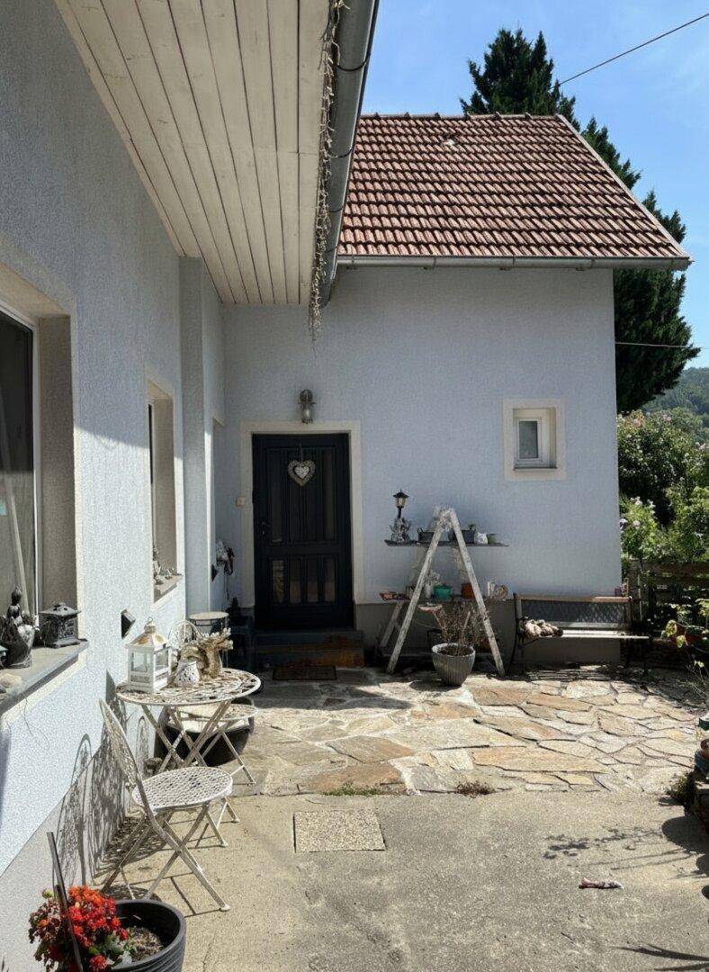 Einladender Eingangsbereich mit gepflasterter Terrasse und Gartenmöbeln.