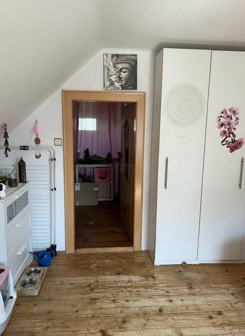 Innenraum mit Holzboden, Dachschräge und weißem Kleiderschrank.