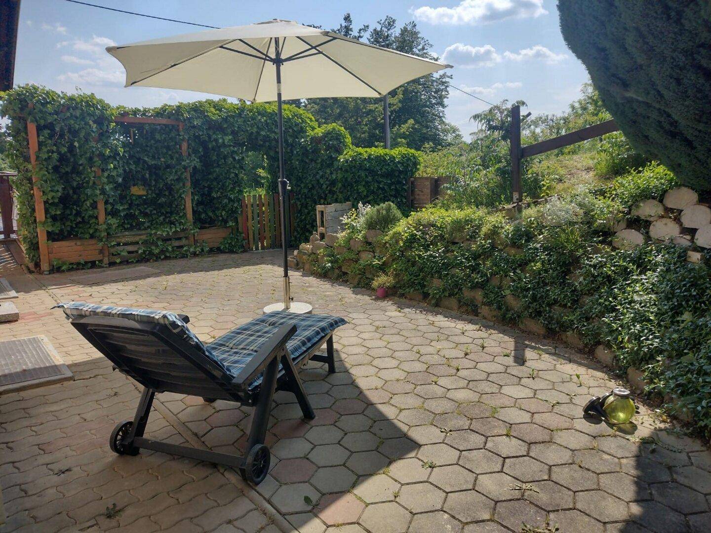 Geräumige gepflasterte Terrasse mit Sonnenliege und Sonnenschirm, ideal zum Entspannen im Freien.