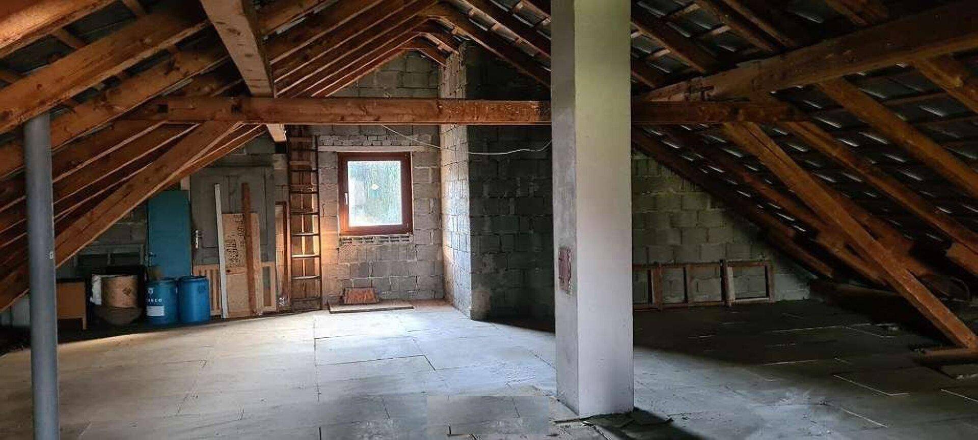 Geräumiger Dachboden mit sichtbaren Holzbalken und einem Fenster für natürliches Licht.