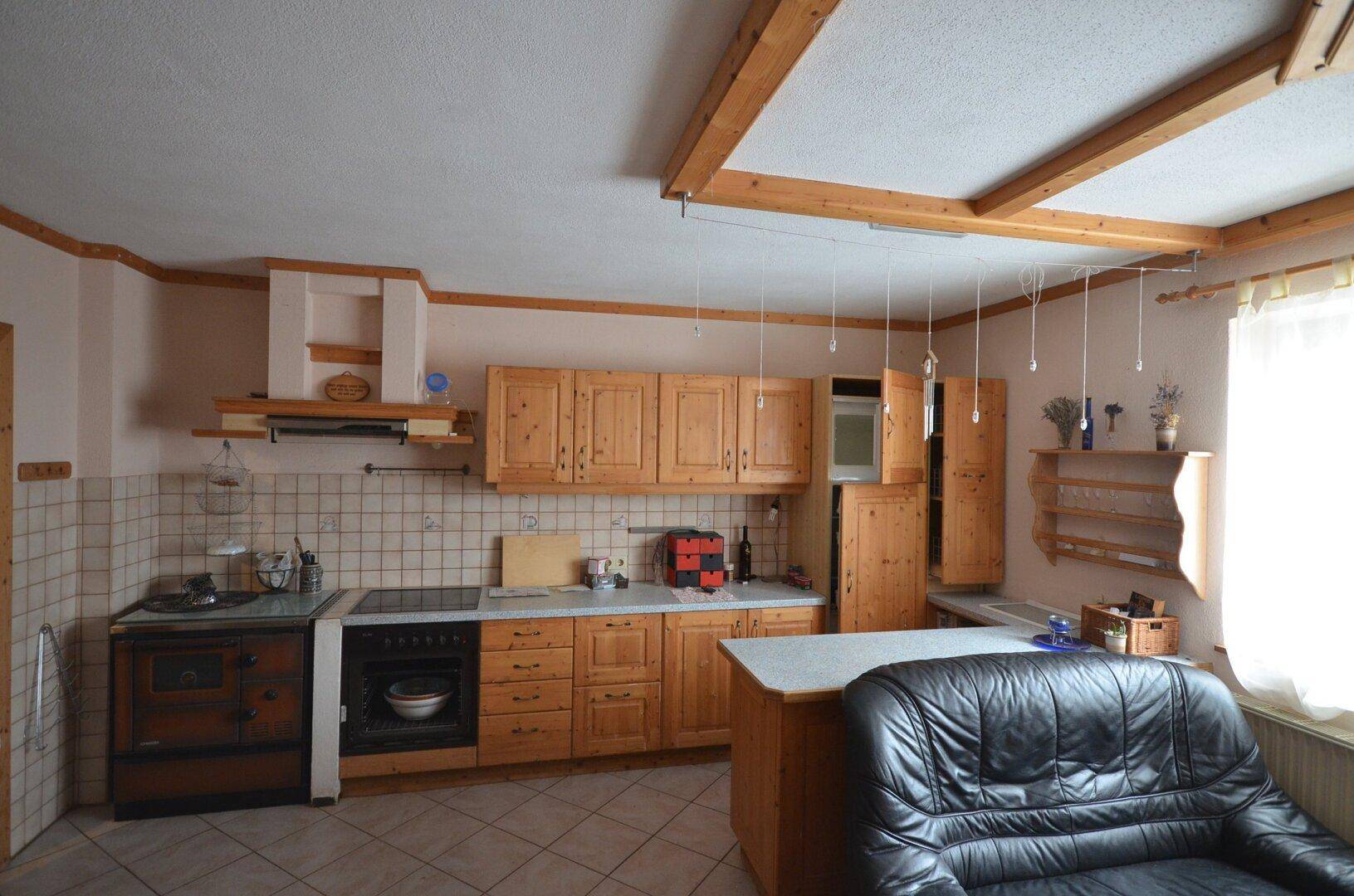 Rustikale Küche mit Holzschränken, Fliesenboden und traditionellem Holzofen.