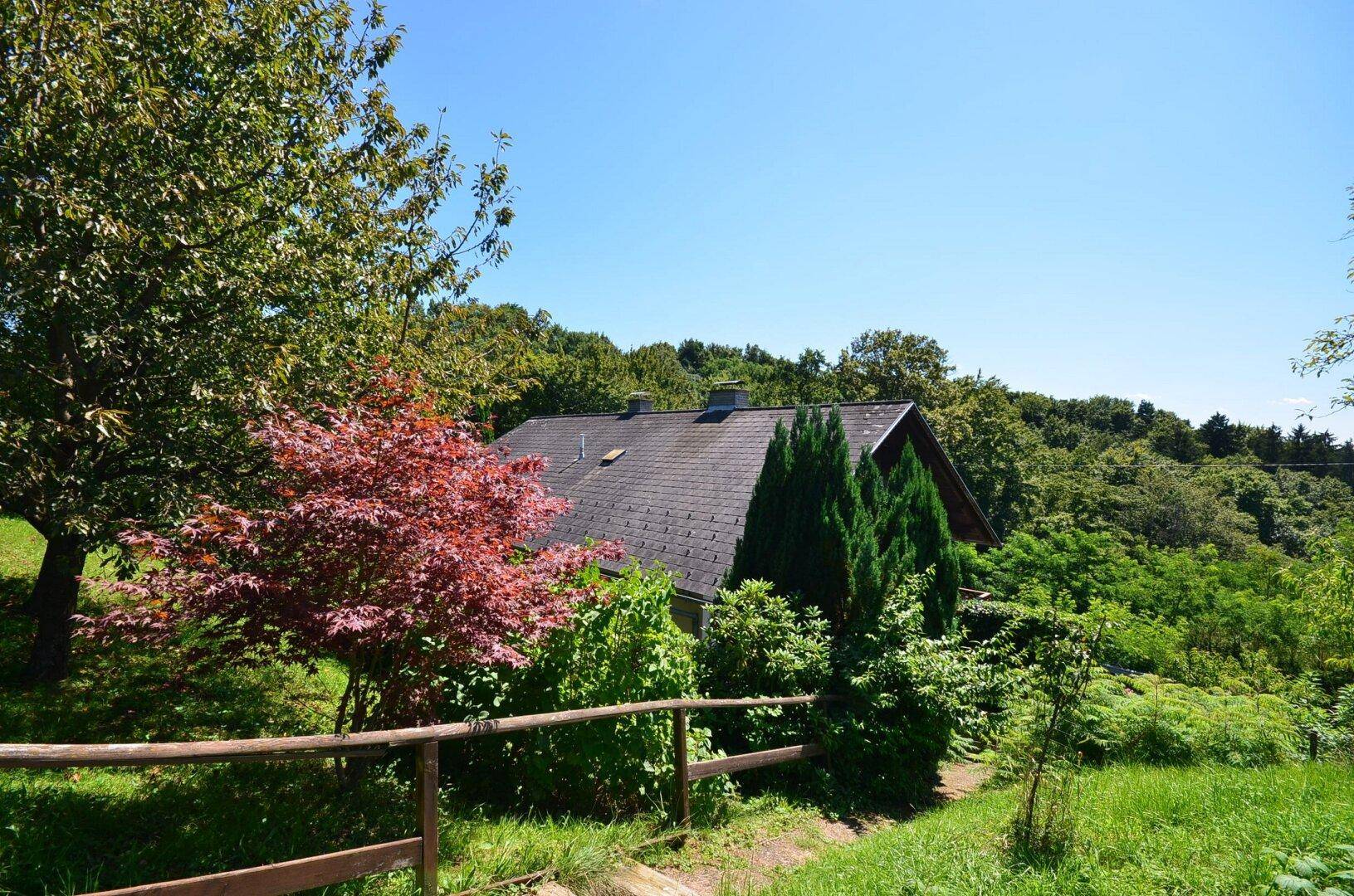 Haus eingebettet in eine grüne Hügellandschaft mit altem Baumbestand.