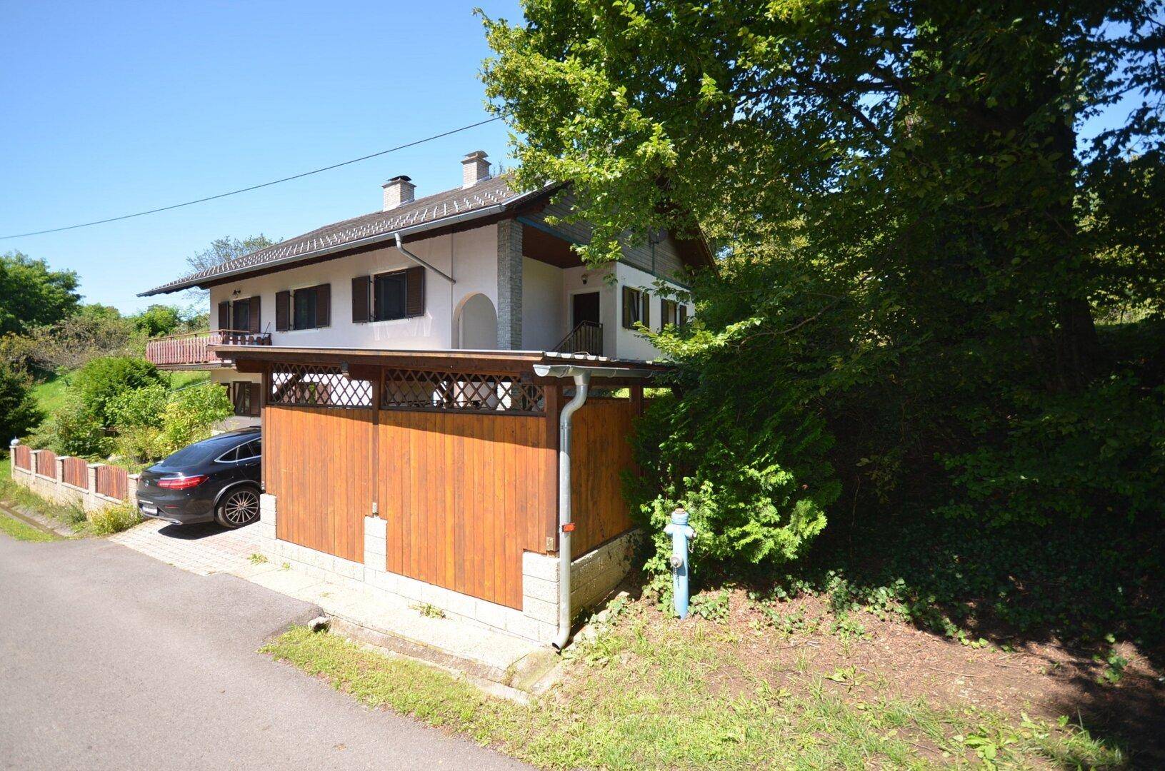 Hausansicht von der Straße mit Carport und einem geparkten Fahrzeug.
