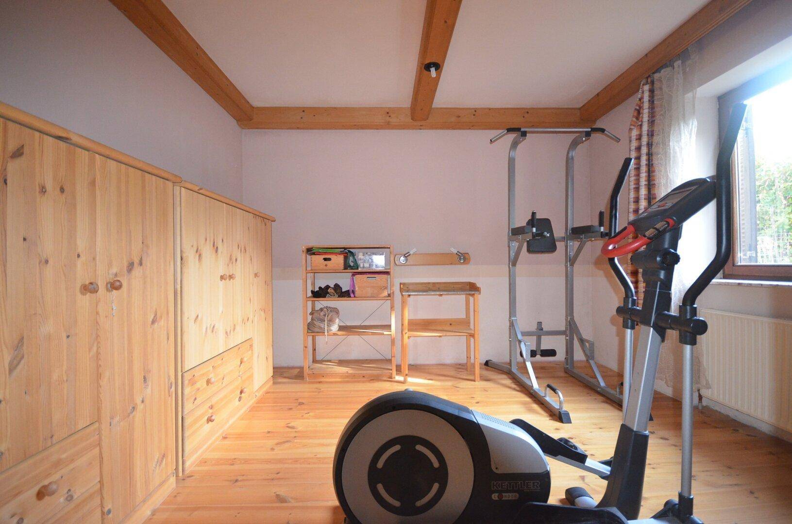 Fitnessraum mit Holzboden, Holzdecke und verschiedenen Trainingsgeräten.