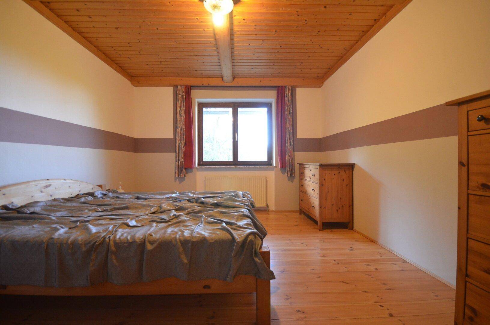 Gemütliches Schlafzimmer mit Holzboden, Holzdecke und traditionellen Möbeln.