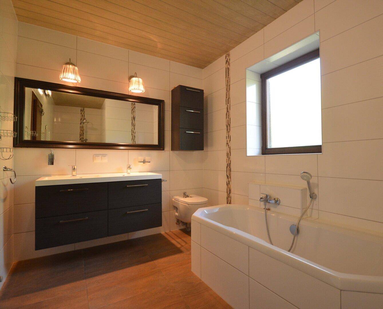 Modernes Badezimmer mit Doppelwaschbecken, Badewanne und Fenster für Tageslicht.