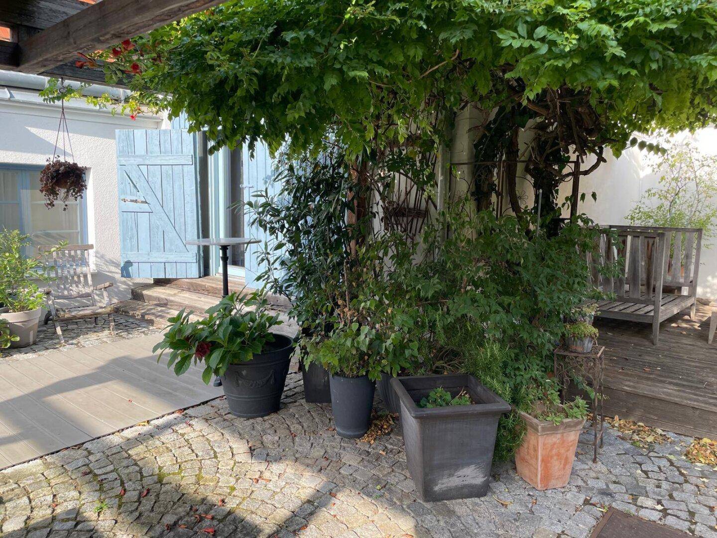 Begrünter Innenhof mit Pflanzen, Holzboden und überdachtem Sitzbereich.