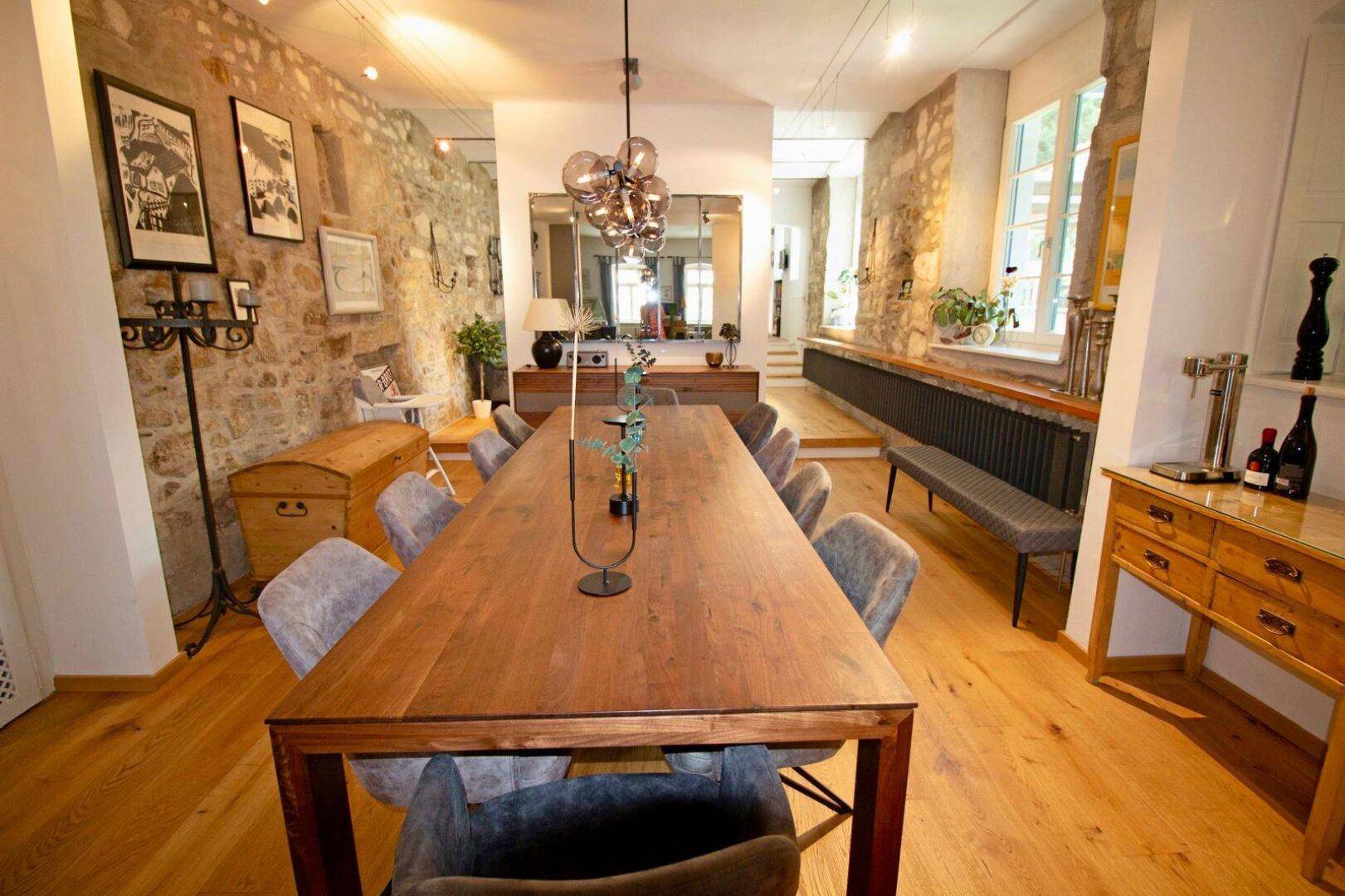 Großzügiger Essbereich mit langem Holztisch, Sitzbank und Natursteinwand.