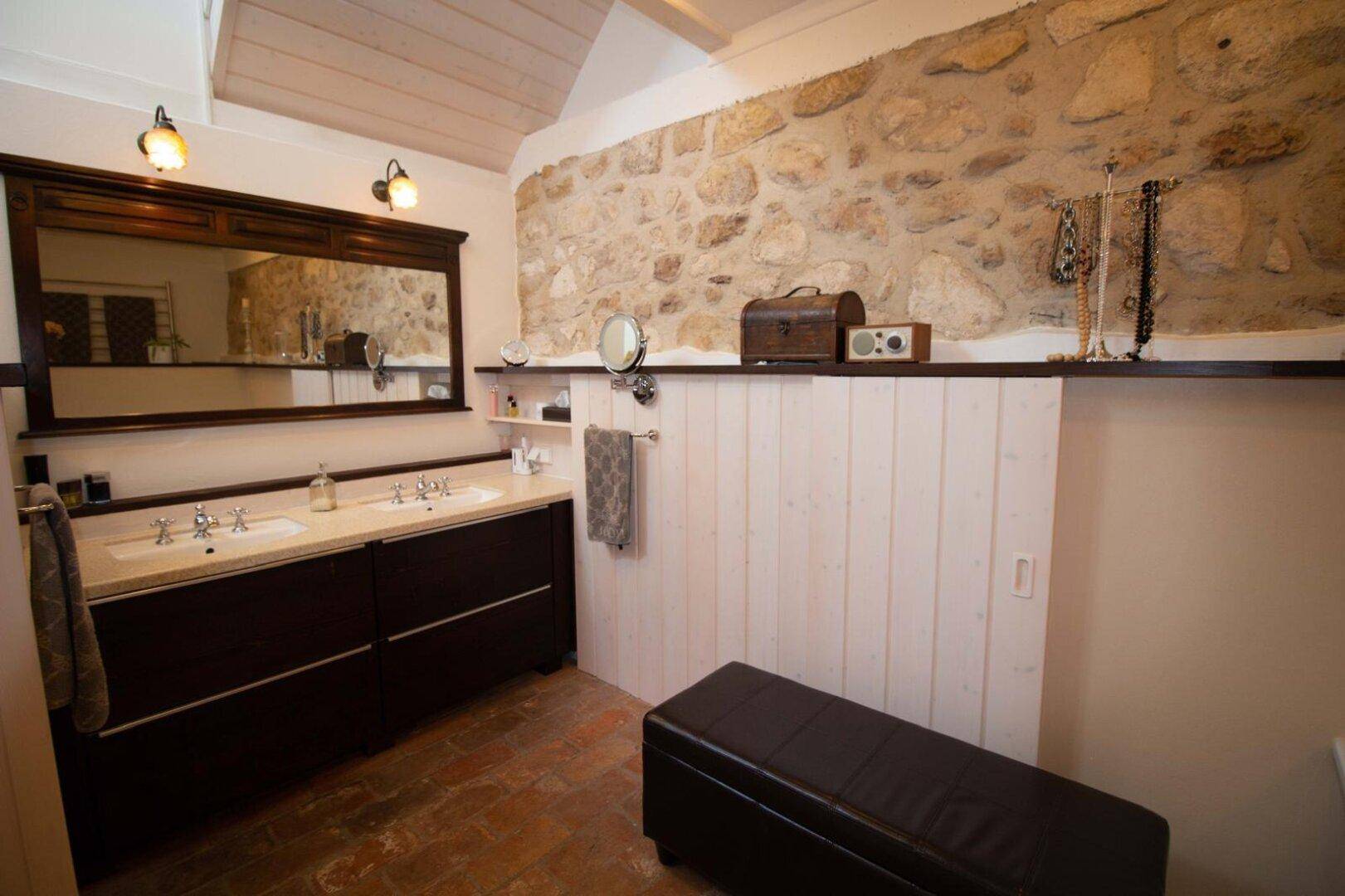 Badezimmer mit Doppelwaschbecken, großem Spiegel und Natursteinwand.