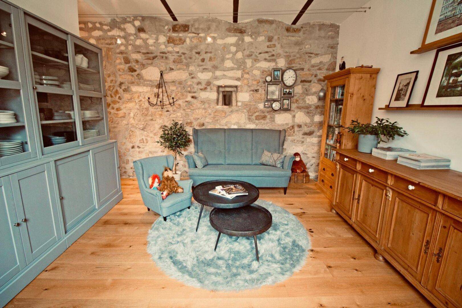 Wohnzimmer mit Natursteinwand, blauen Möbeln und Holzboden.