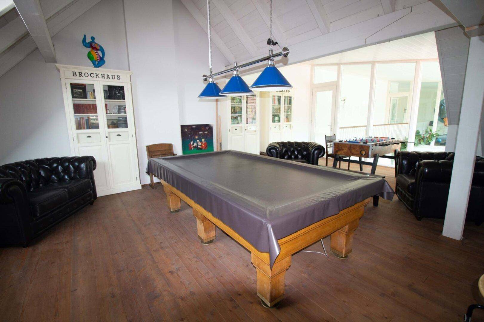 Geräumiges Spielzimmer mit Billardtisch, Ledersofas und Holzboden.