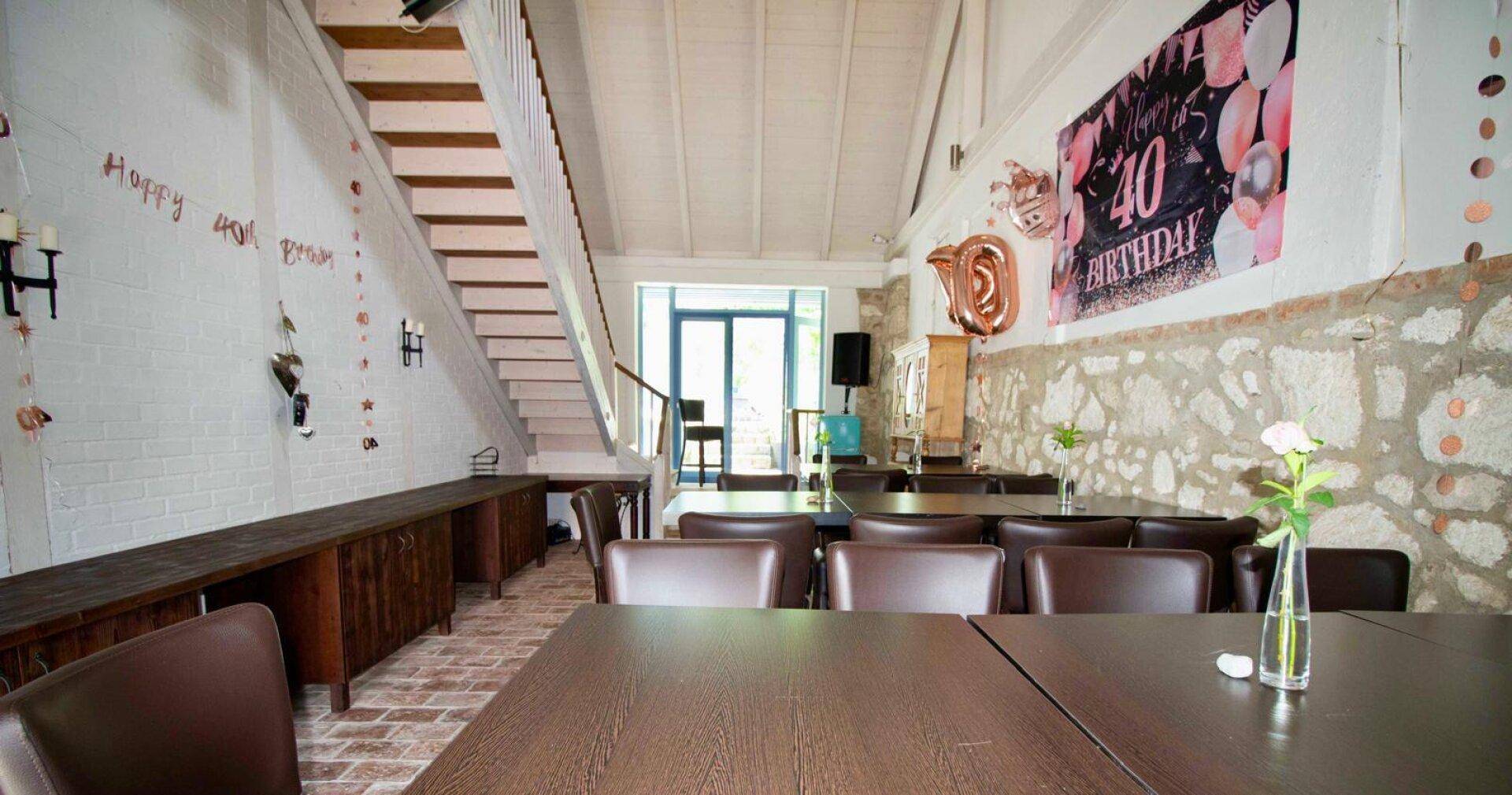Großer Raum mit Tischen, Stühlen und Treppe, dekoriert für eine Feier.
