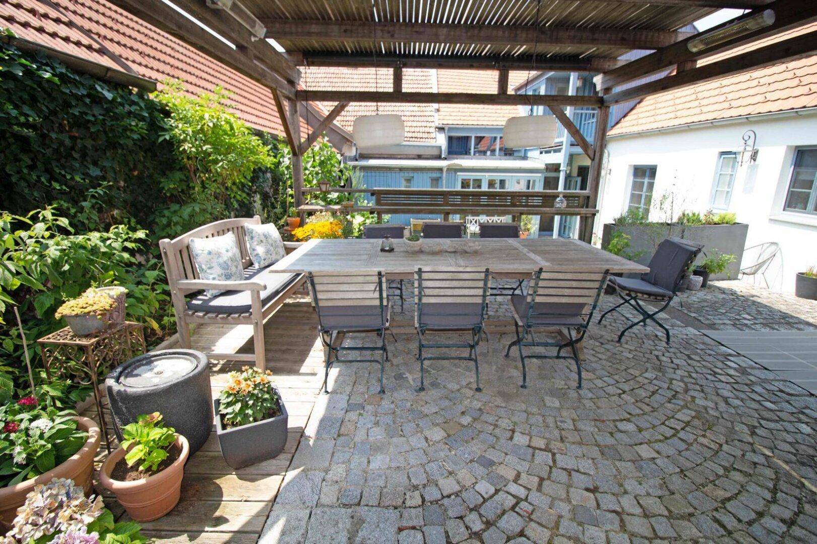 Große Terrasse mit Holztisch, Gartenmöbeln und Pergola im Außenbereich.