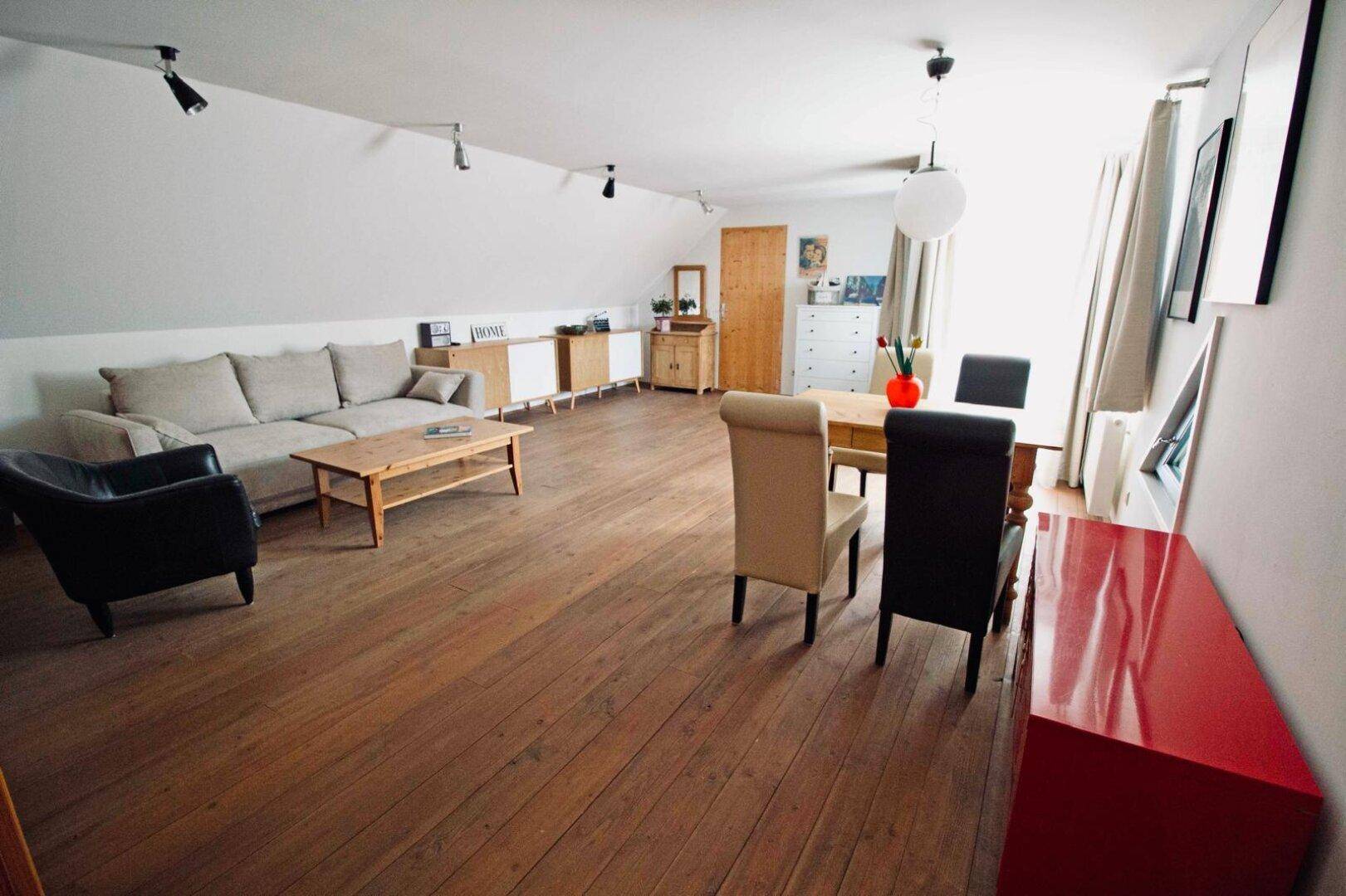 Geräumiges Wohnzimmer im Dachgeschoss mit Holzdielenboden, gemütlichem Sofa und Essbereich.