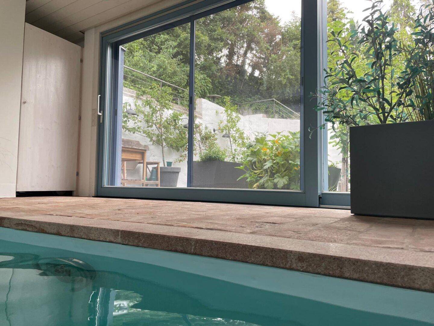 Innenpoolbereich mit großen Glasschiebetüren und Blick auf die begrünte Außenanlage.