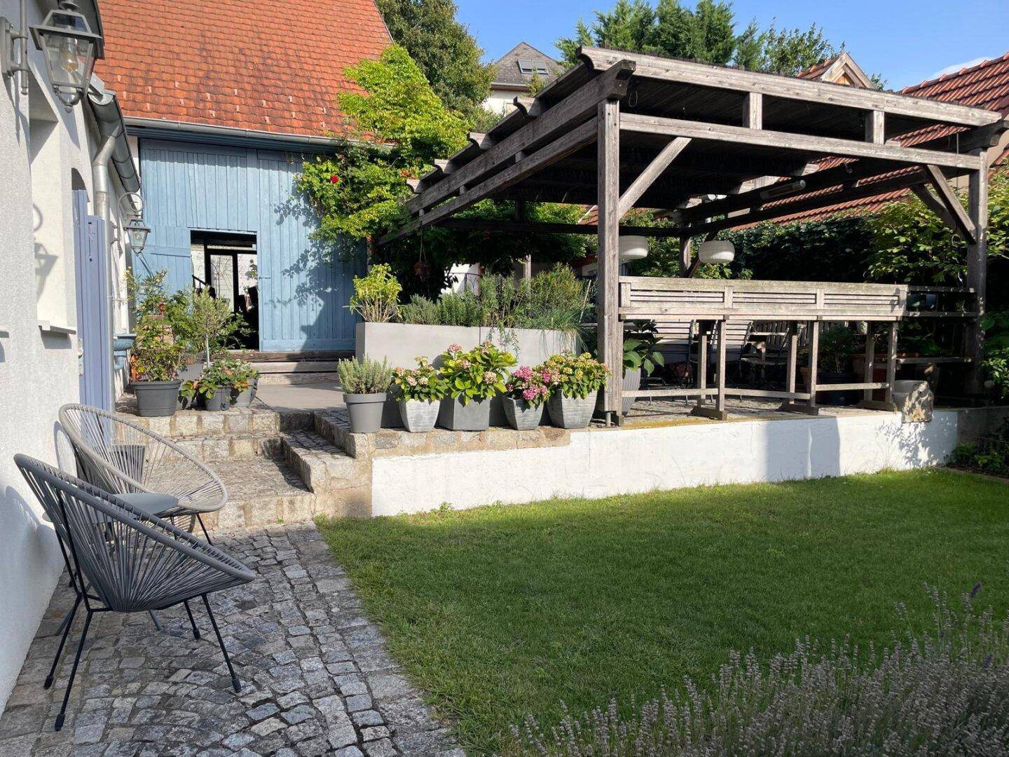 Gepflegter Garten mit Rasenfläche, Kopfsteinpflaster und einer Holzpergola im Hintergrund.