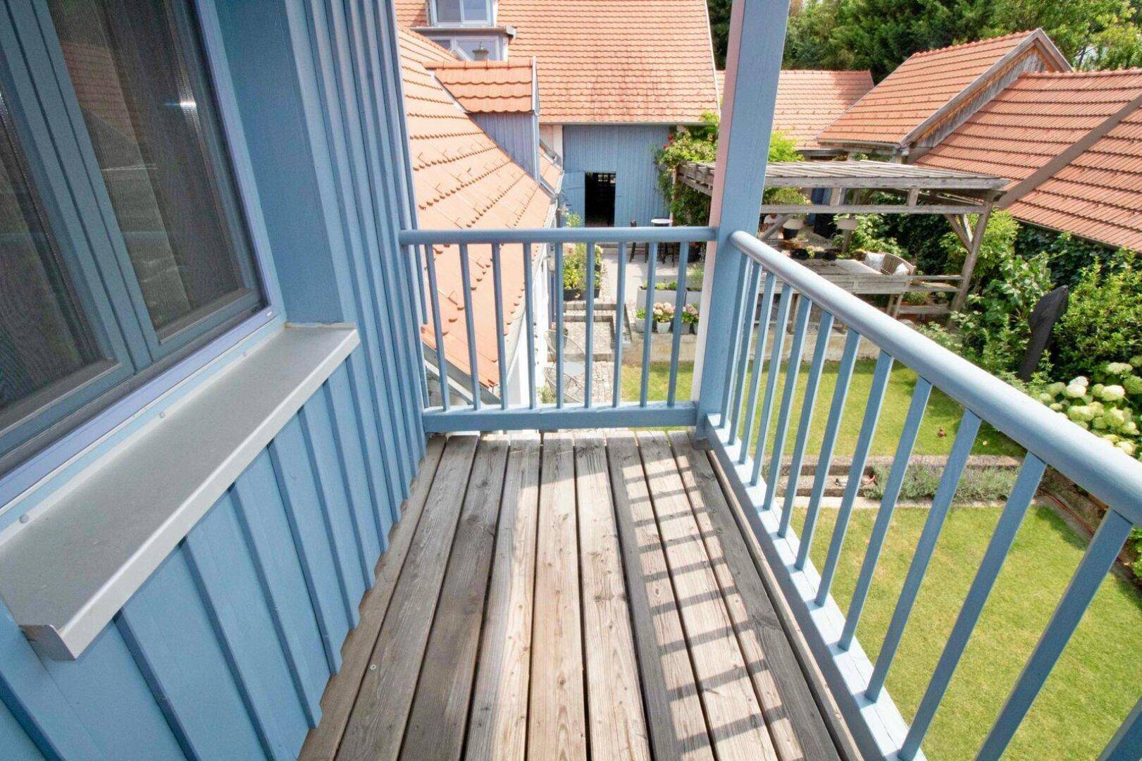 Kleiner Holzbalkon mit blauer Holzverkleidung und Blick auf den grünen Gartenbereich.