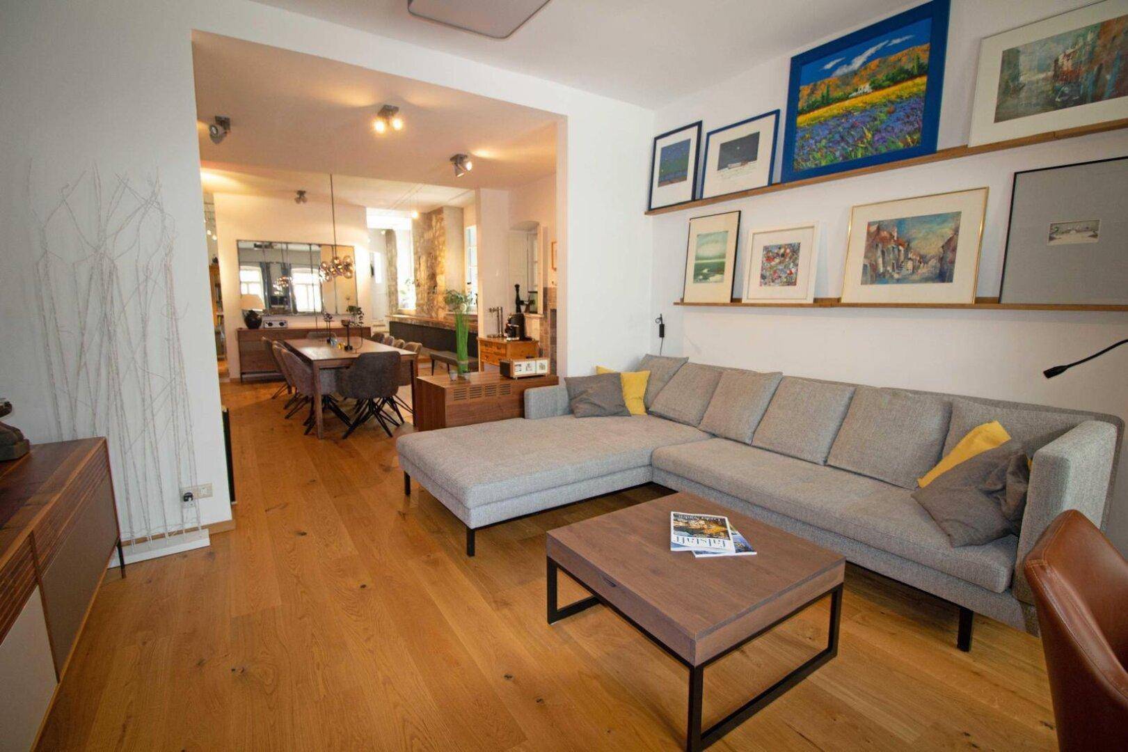 Heller offener Wohn-Essbereich mit Eichenparkett, modernem Sofa und Kunstwerken an der Wand.