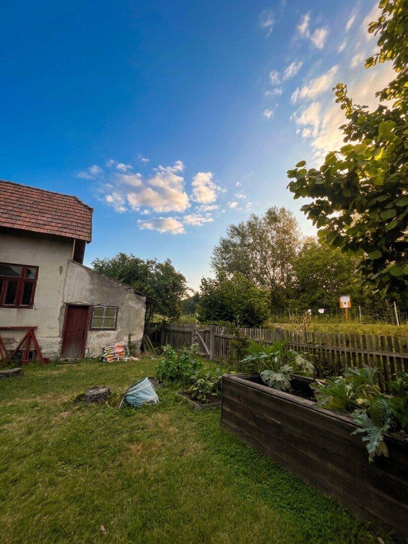 Weitläufiger Gartenbereich mit Hochbeet und Holzzaun, unter einem weiten blauen Himmel mit vereinzelten Wolken.