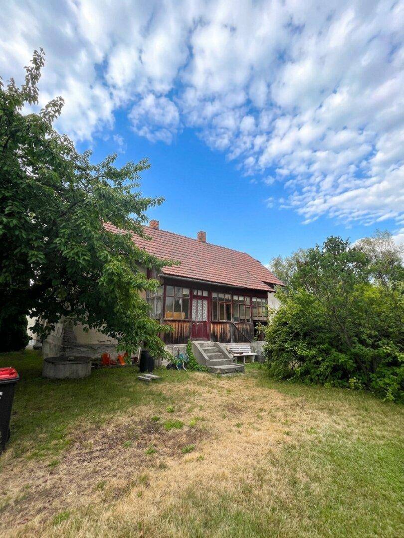 Gesamtaufnahme des alten Wohnhauses von der Gartenseite, mit verglaster Veranda und rustikalen Betonstufen.