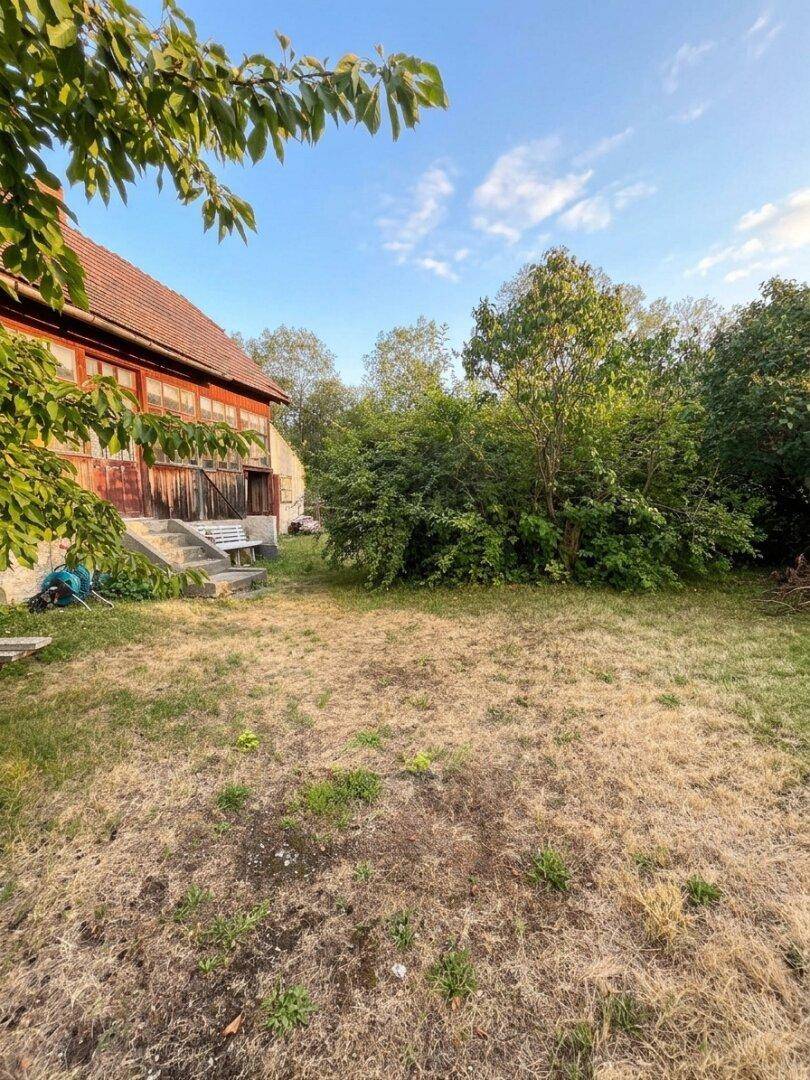 Gartenbereich mit trockener Rasenfläche und Blick auf die Seite des Wohnhauses mit der verglasten Veranda.