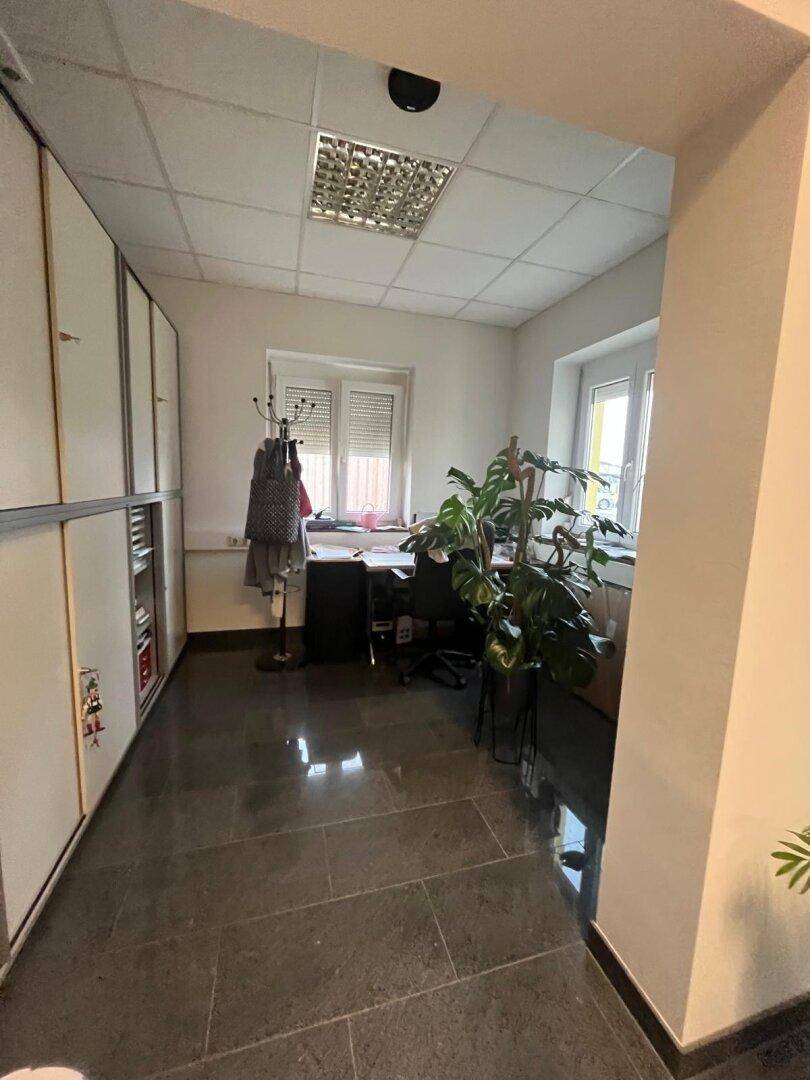 Helles Büro mit dunklem Fliesenboden, weißen Wänden, Einbauschränken und einem Schreibtisch.