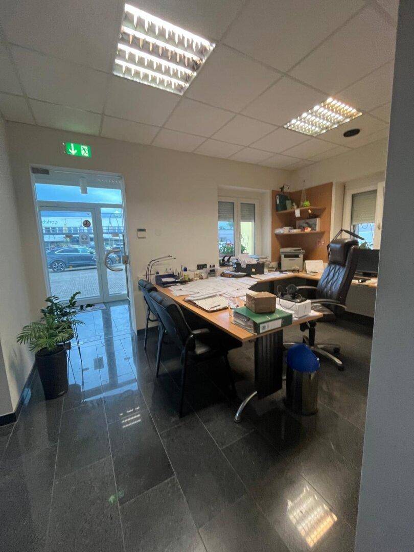 Geräumiges Büro mit dunklem Fliesenboden, großem Schreibtisch und Blick auf den Eingangsbereich.