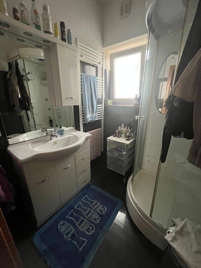 Badezimmer mit Duschkabine, Waschtisch, Spiegel und einem Fenster für natürliches Licht.