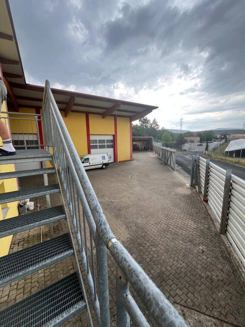 Außenansicht eines Industriegebäudes mit gelber Fassade, Metalltreppe und Zufahrtsbereich.