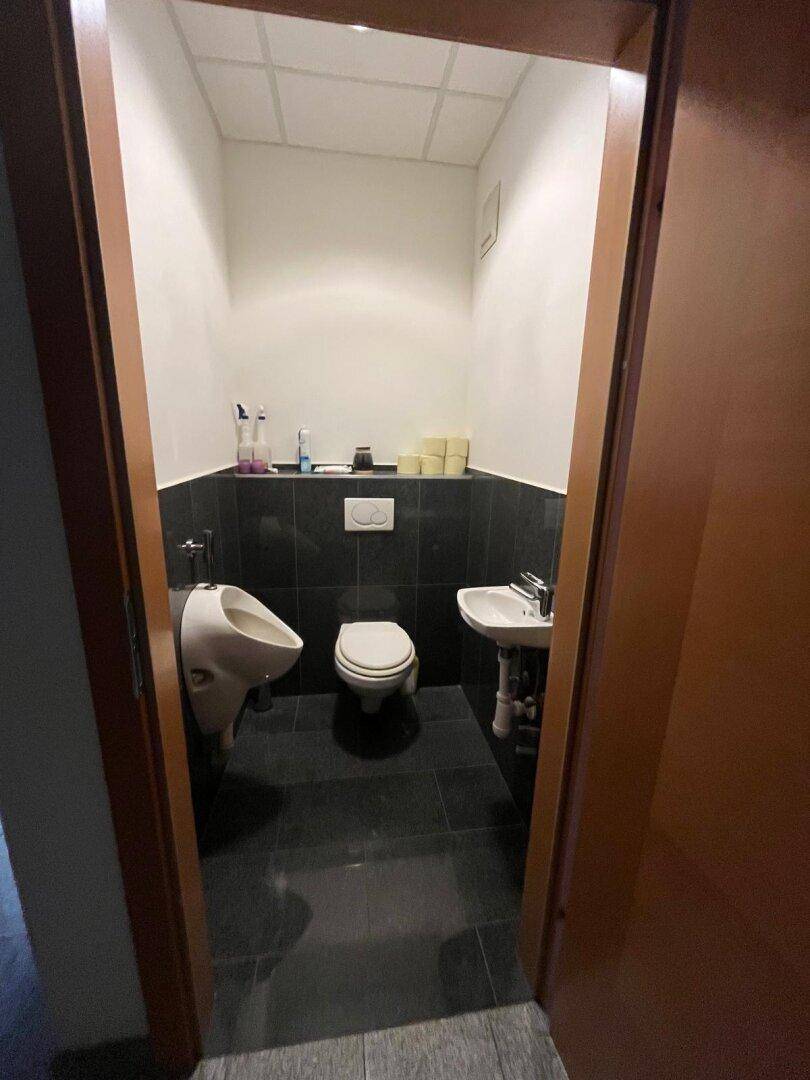 Gästetoilette mit WC, Urinal und kleinem Waschbecken, ausgestattet mit dunklen Fliesen.