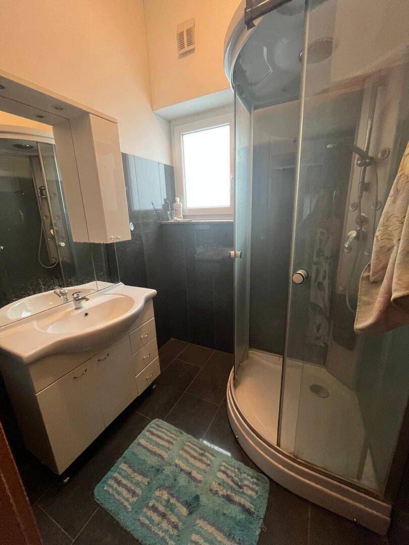 Badezimmer mit Duschkabine, Waschtisch, Spiegel und einem Fenster für natürliches Licht.