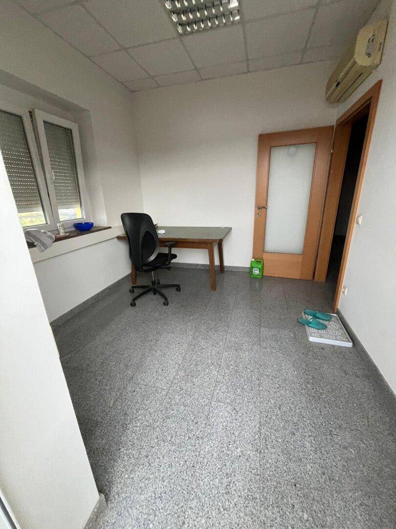 Leeres Büro mit grauem Fliesenboden, weißen Wänden, Fenster und einer Klimaanlage.