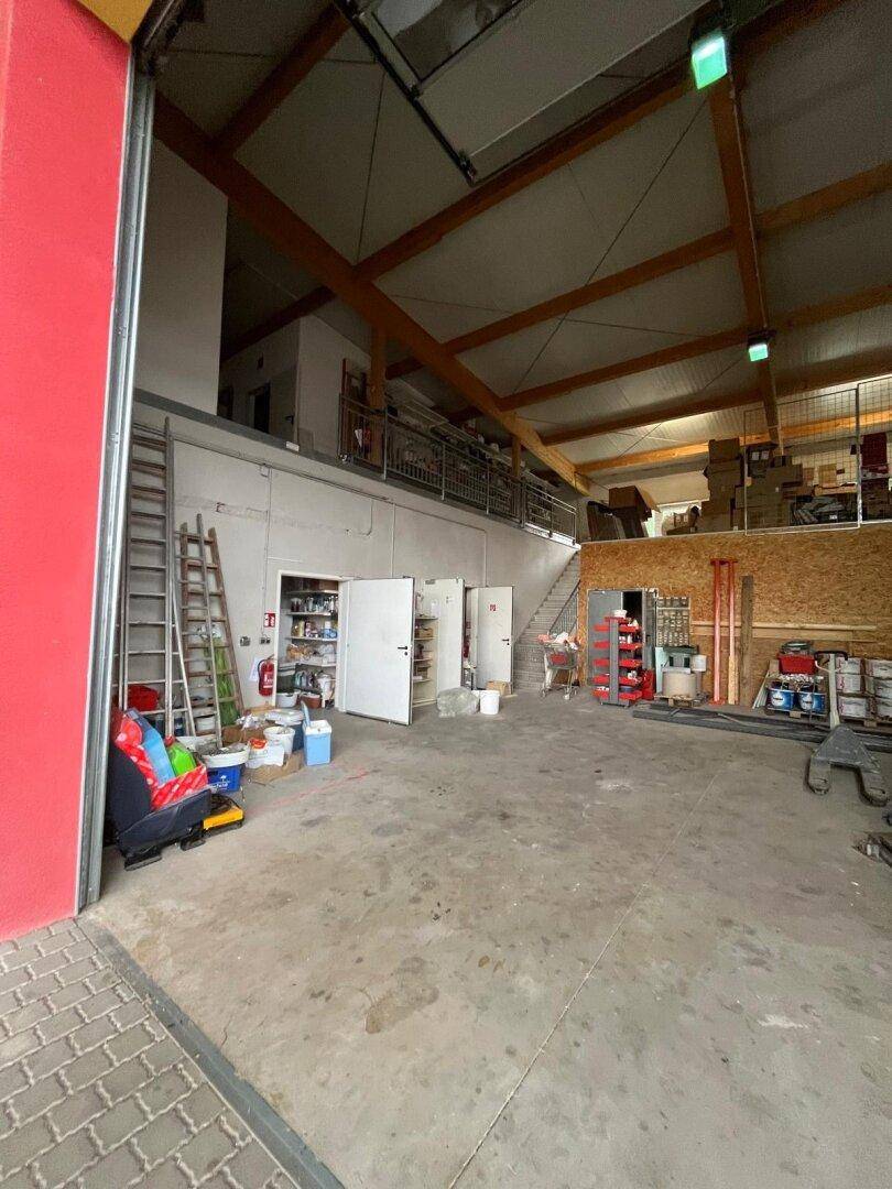 Große Lagerhalle mit Betonboden, hohen Decken und einem geöffneten Rolltor zur Außenseite.