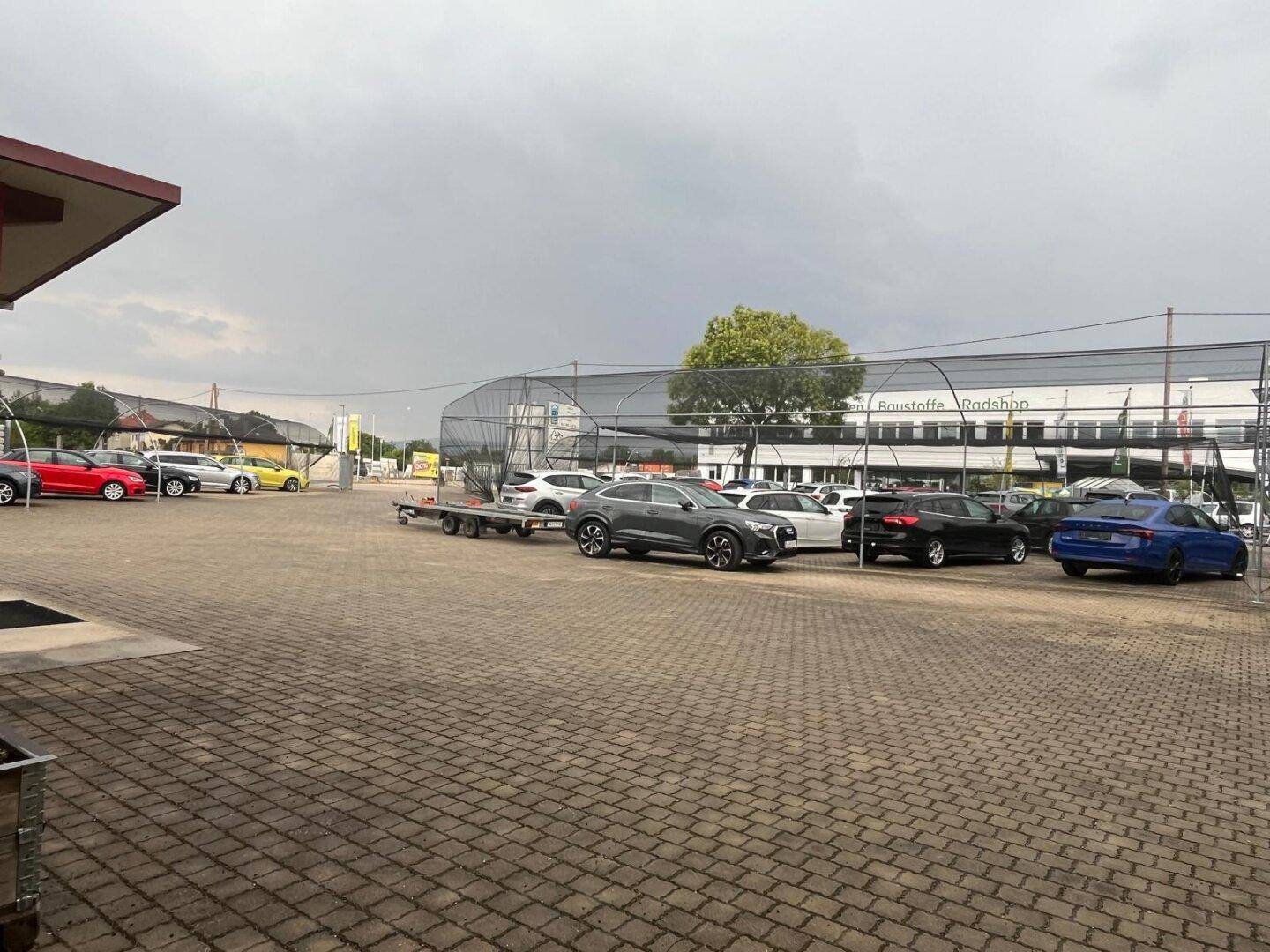 Großer Außenparkplatz mit gepflastertem Boden und mehreren geparkten Autos unter bewölktem Himmel.