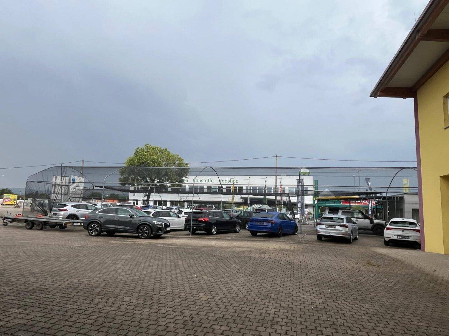 Weitläufiger Außenparkplatz mit gepflastertem Boden und verschiedenen Fahrzeugen unter einem bewölkten Himmel.