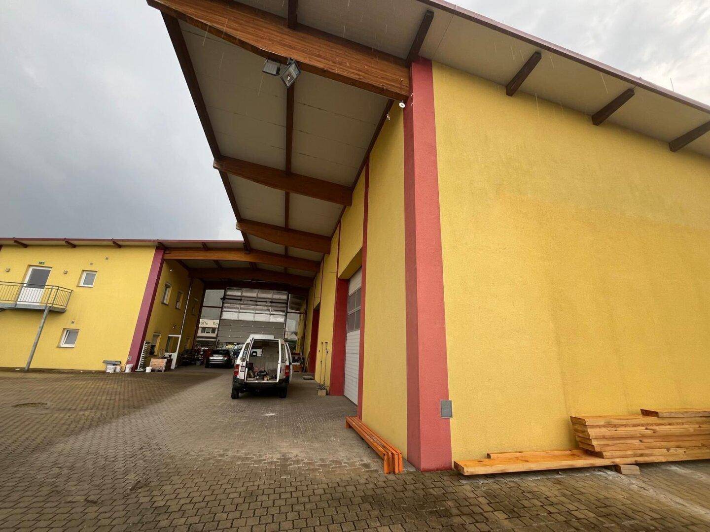 Gelb gestrichenes Industriegebäude mit rotem Akzentstreifen und großem Einfahrtstor unter bewölktem Himmel.