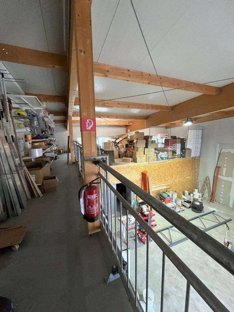 Blick von einer Galerie in eine Lagerhalle mit Holzbalken, Kartons und Baumaterialien.