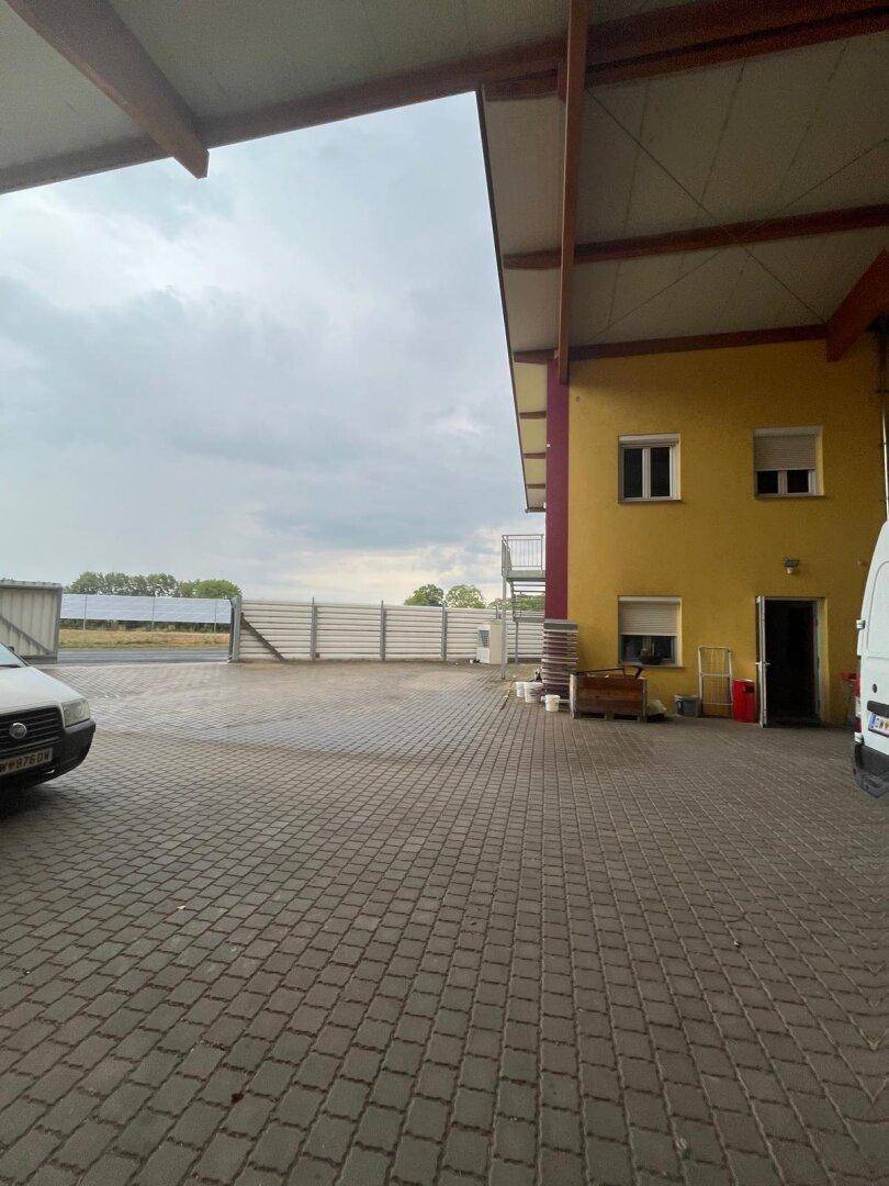 Gepflasterter Außenbereich neben einem Gebäude mit hoher Metallzaunbegrenzung unter bewölktem Himmel.