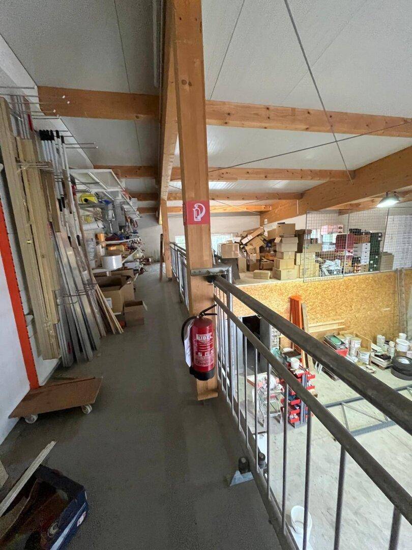 Blick von einer Galerie in eine Lagerhalle mit Holzbalken, Kartons und Baumaterialien.
