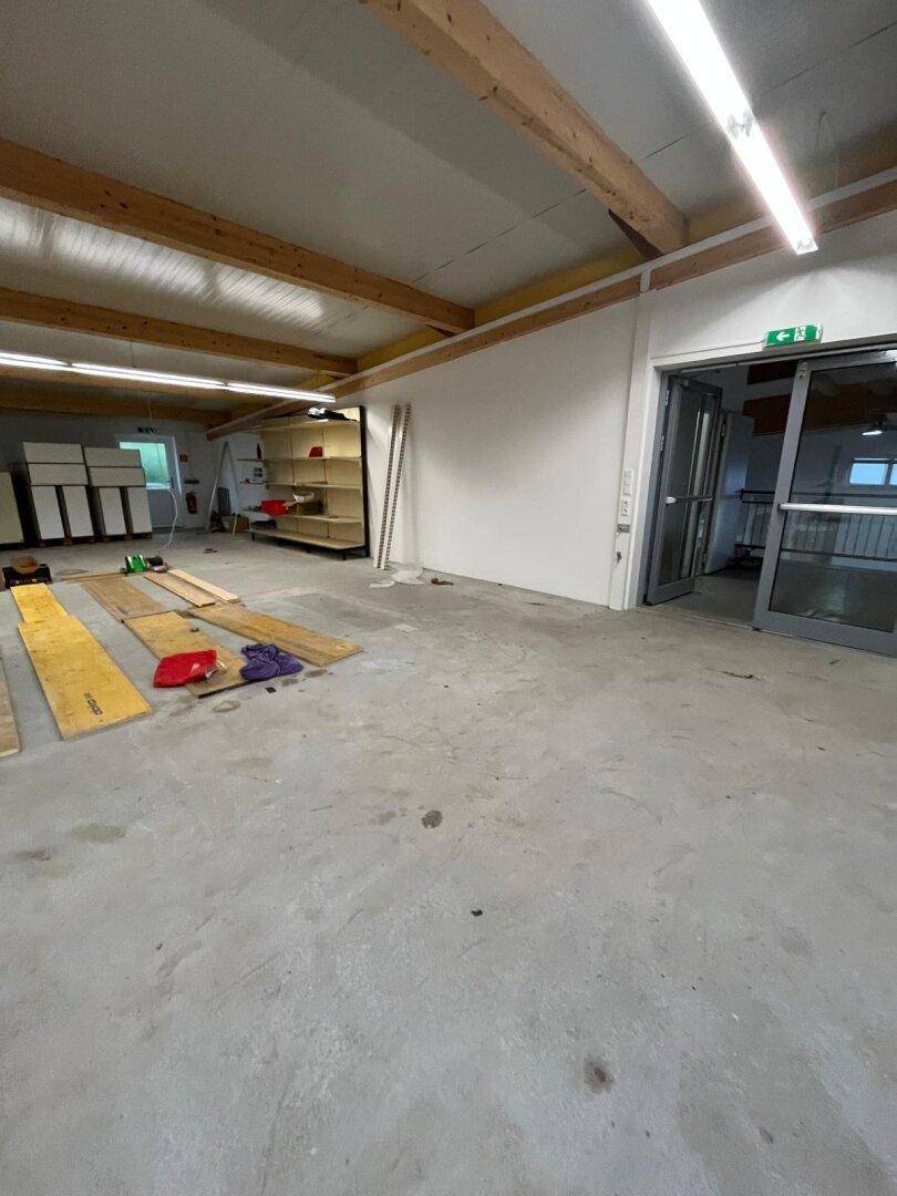 Große Lagerhalle mit Betonboden, Holzbalken und einem Eingangsbereich mit Glastüren.