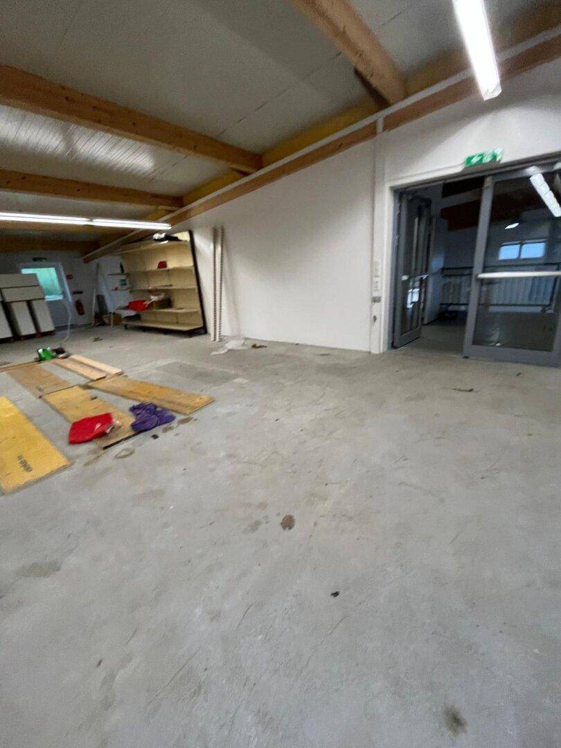 Große Lagerhalle mit Betonboden, Holzbalken und einem Eingangsbereich mit Glastüren.